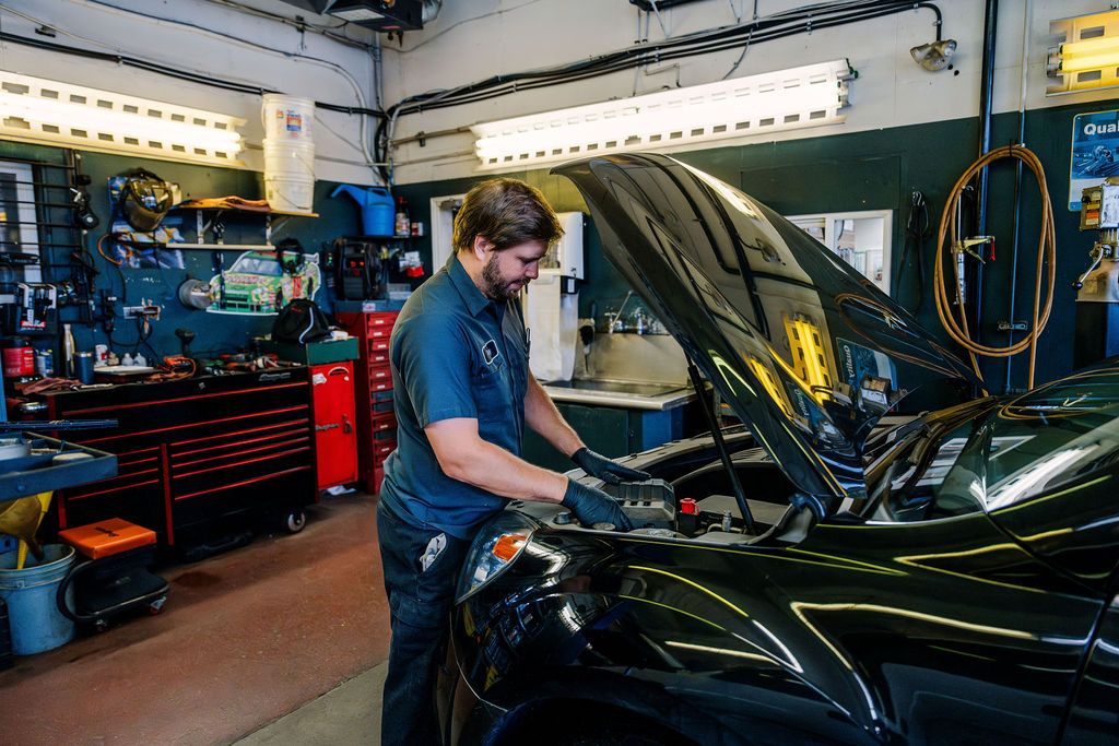 A technician in gloves working under the open hood of a black car in the service bay