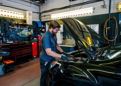 A technician working under the hood of a black car