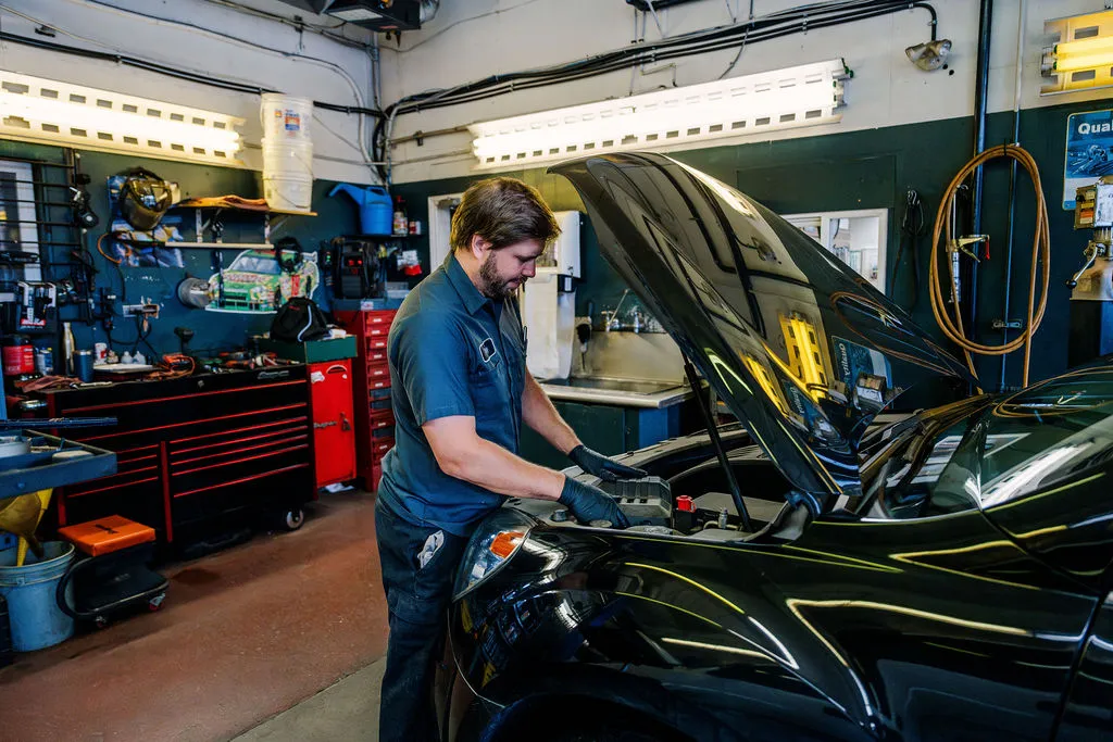 A technician working under the hood of a black car in one of the service bays
