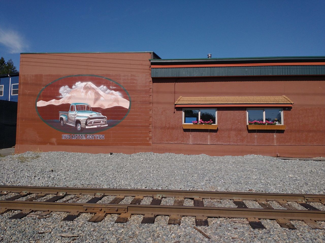 A mural of a vintage pickup truck with a 1954 licence plate and a snowy mountain, painted on the side wall of the shop beside the railway tracks.