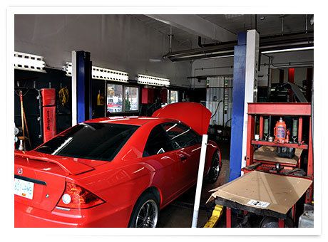 A red car with its hood up in one of the service bays