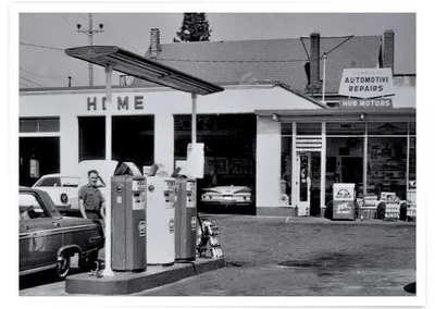 An attendant at the pumps, with the Hub Motors repair shop behind, in black and white