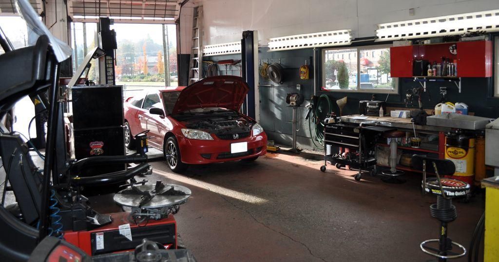 A tire changing machine in the foreground of one of the shop's service bays, with a red car behind it with its hood up