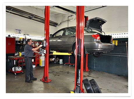 A technician beside a car raised on a hoist in one of the service bays