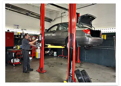 A technician beside a car raised on a hoist